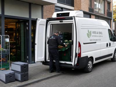 Voor een winkel laadt een koelwerkbus verse kratten voor dagelijks gekoeld vervoer aan de stoeprand.