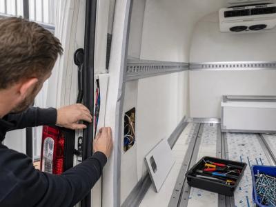 Technische handen werken aan de isolatie en bekabeling van een koelwagen in opbouw.