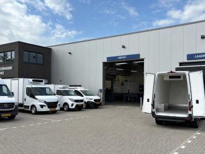 Een industriële voorhof met bedrijfsauto's voor gekoeld transport, een open servicebay en een open laadruimte bij de ombouwlocatie.