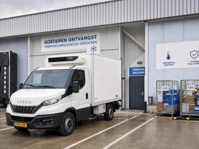 An IVECO Daily koelwagen stands at a logistics yard beside loading bays and a service entrance.