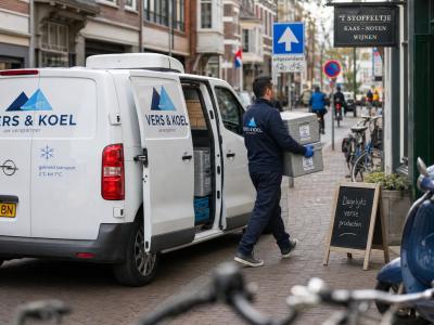 Een compacte koelwagen staat aan een stadsstoep terwijl een chauffeur gekoelde kratten naar een winkel brengt tijdens een drukke stadsroute.