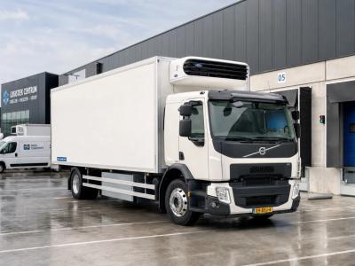 Een transporter koelwagen staat geparkeerd op een logistiek terrein bij laadperrons en andere bestelwagens.