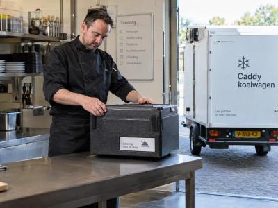 Een cateraar controleert een afgesloten voedselcontainer bij de achteringang, terwijl een Caddy koelwagen klaarstaat voor gekoelde stadsleveringen.