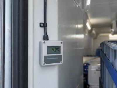Een temperatuursensor aan de geïsoleerde wand van een elektrische koelbus meet de omstandigheden naast een gezekerde transportkrat.