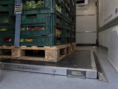 Zware kratten staan vastgezet in een koelbestelwagen, met de wielkast en geïsoleerde wand zichtbaar bij de vloer.