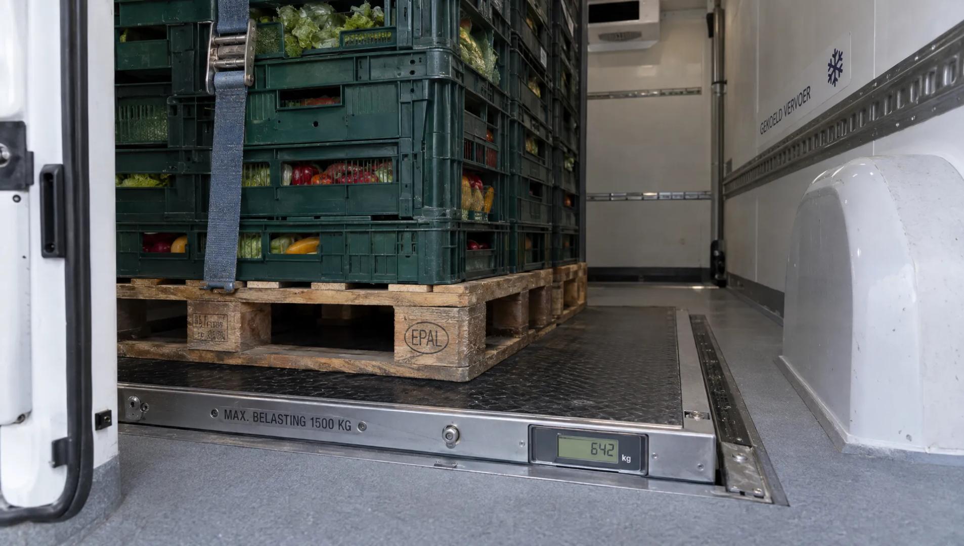 Zware kratten staan vastgezet in een koelbestelwagen, met de wielkast en geïsoleerde wand zichtbaar bij de vloer.