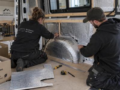 Technici passen isolatiepanelen rond de wielkast van een bestelwagen tijdens de voorbereiding van een koelombouw.