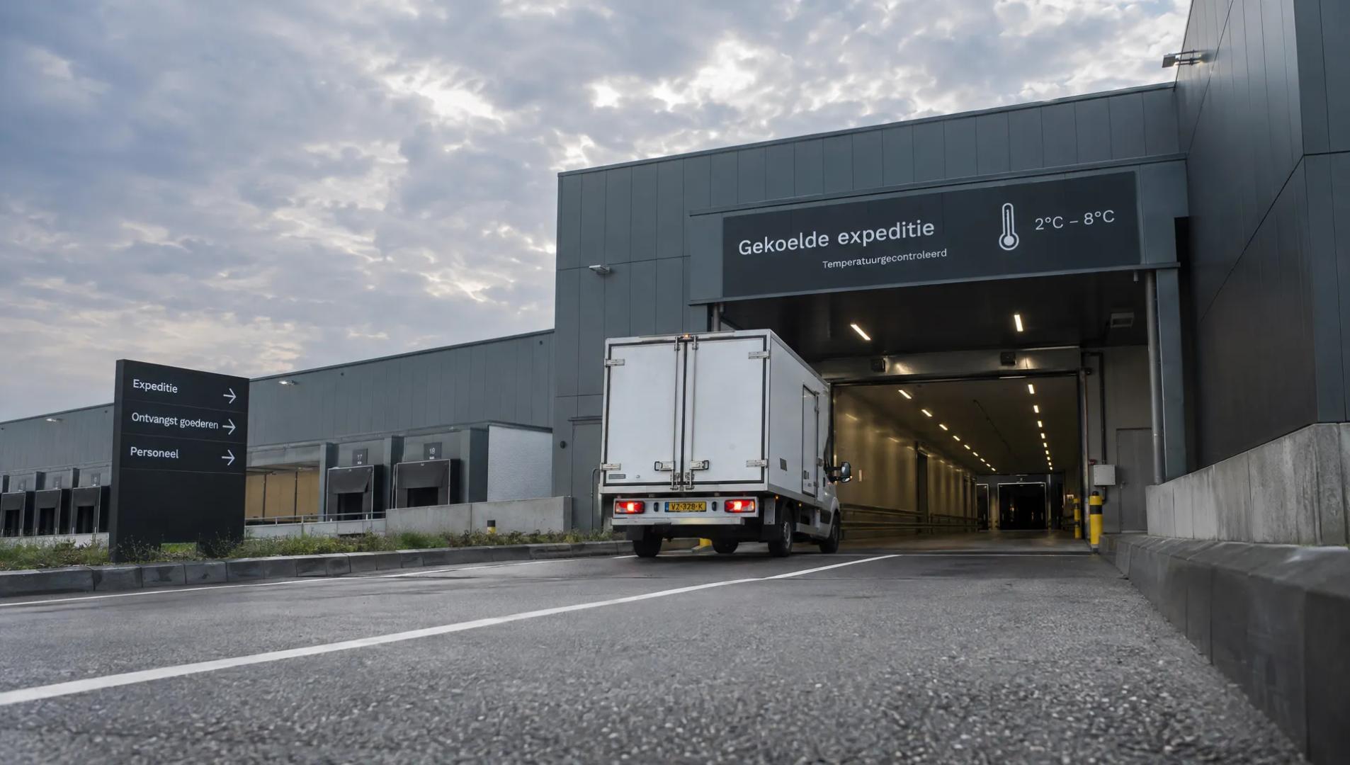 Een koelwagen rijdt een overdekte laadzone binnen bij een distributiegebouw.