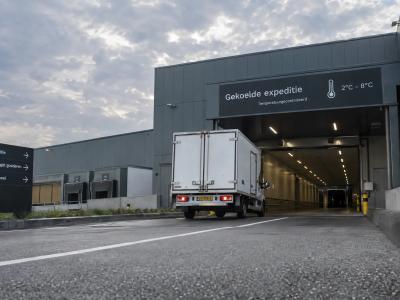 Een koelwagen rijdt een overdekte laadzone binnen bij een distributiegebouw.