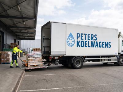 Een Peters-koelwagen staat bij een laadperron terwijl een medewerker pallets met goederen op de laadklep zet voor bezorging.