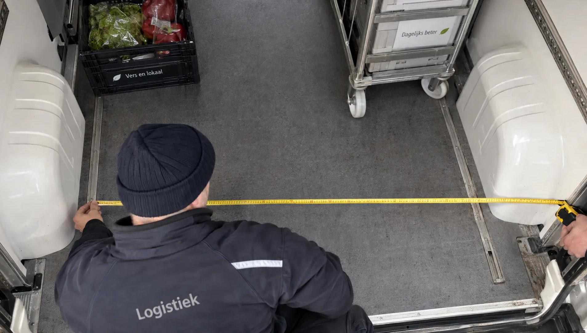 Een medewerker meet de breedte tussen de wielkasten van een koelbus om te controleren of de lading past.