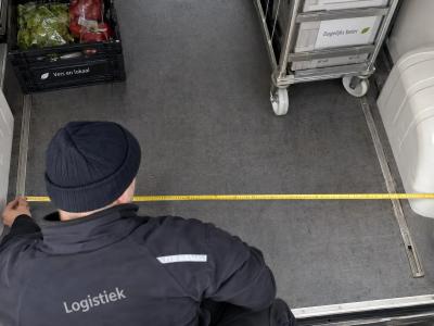 Een medewerker meet de breedte tussen de wielkasten van een koelbus om te controleren of de lading past.